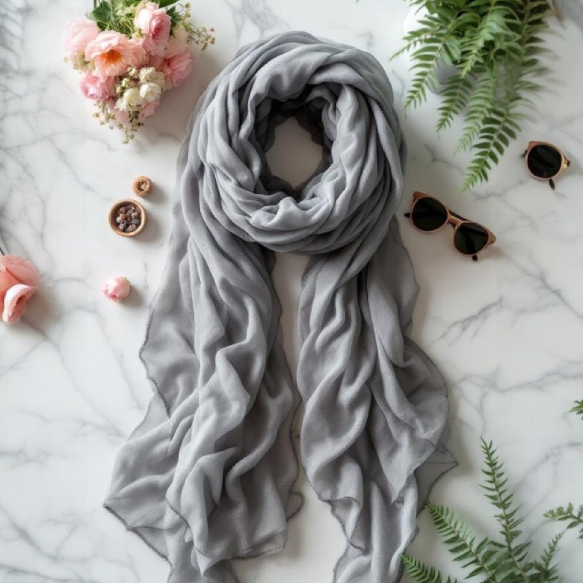 Soft gray chiffon scarf draped elegantly on a marble surface with flowers and sunglasses.