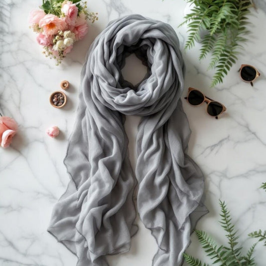 Soft gray chiffon scarf draped elegantly on a marble surface with flowers and sunglasses.